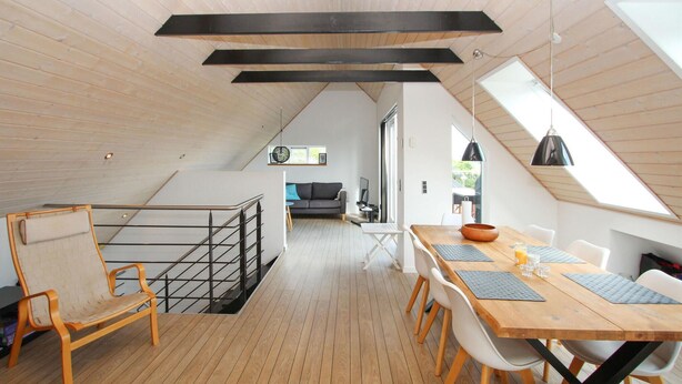 A modern loft with a wooden floor, a dining area with a wooden table and chairs, a sofa, and a staircase with a metal railing. - Beautiful home in Samsø with WiFi (Samsø)