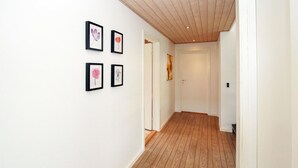 A hallway with wooden flooring and white walls, featuring four framed floral artworks. - Beautiful home in Samsø with WiFi (Samsø)