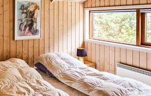 A bedroom with wooden walls, a bed, a nightstand with a lamp, a window with a view of greenery, and a painting on the wall. - 3 bedroom cozy home in Samsø (Samsø)