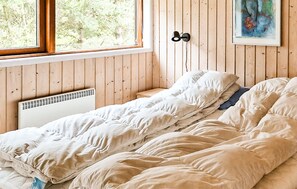 Un lit simple avec une literie blanche, dans une pièce aux murs en bois et dotée d’une fenêtre.
