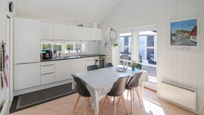 A modern kitchen with white cabinets, a dining table with chairs, and a large window offering a view of the street.