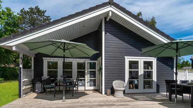 A covered patio area with outdoor furniture and umbrellas, a grill, and a view of the house.