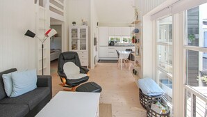 A compact living space with a sofa, a chair, a dining table, a kitchen area, and large windows.