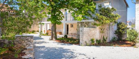 A two-story building with a stone facade, a balcony, and a gravel driveway.