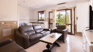 A living room with a brown leather sofa, a wooden coffee table, and a TV on a stand. - Spacious 5-bedroom Villa with pool and barbecue (Can Picafort)
