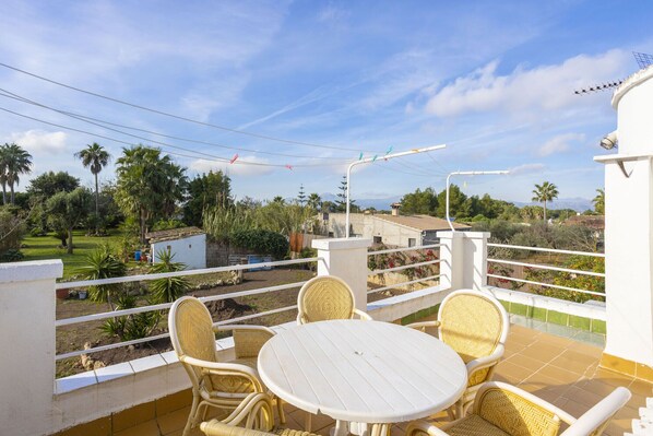 A balcony with wicker furniture and a view of a garden and mountains. - Spacious 5-bedroom Villa with pool and barbecue (Can Picafort)