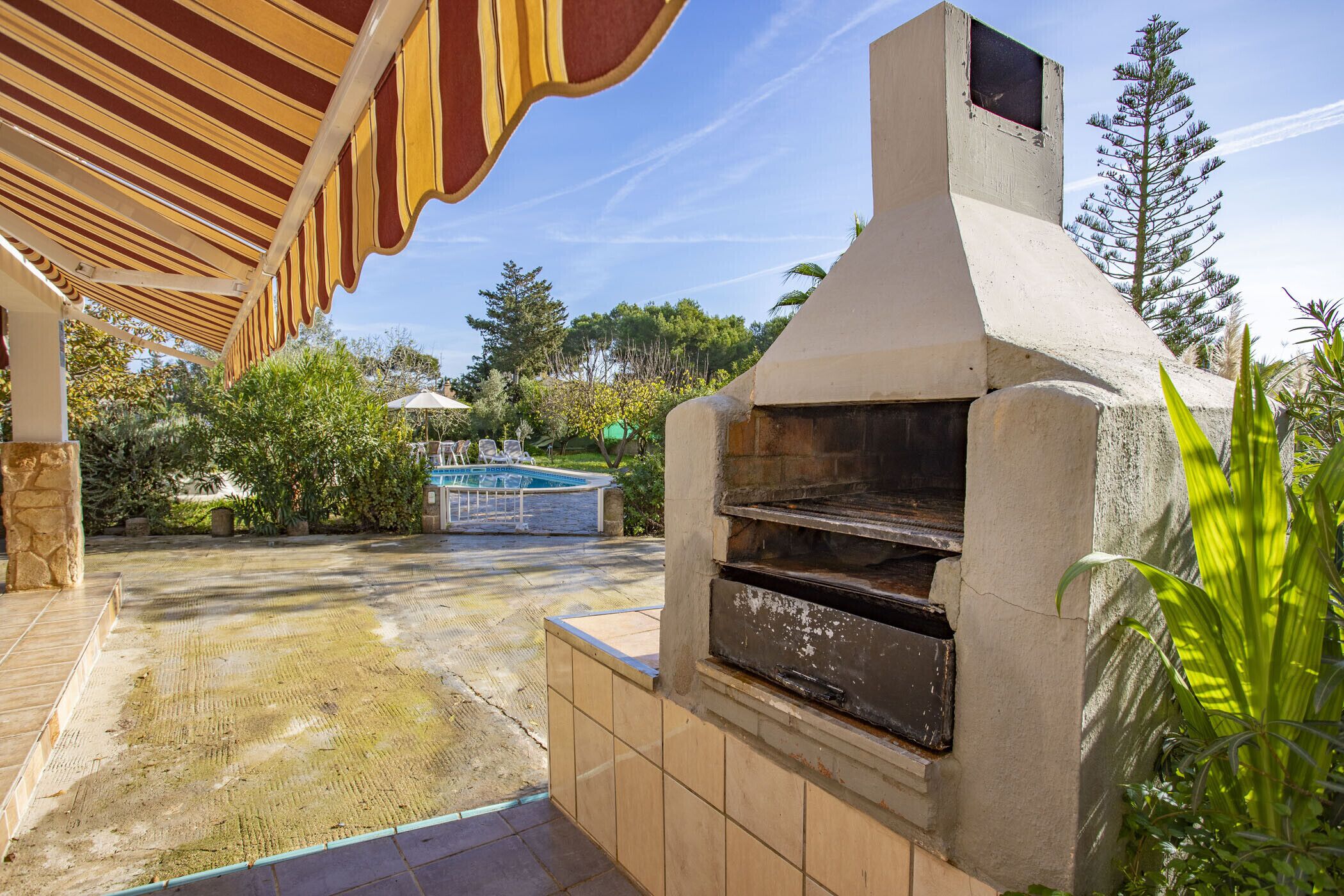 An outdoor patio with a stone floor, a barbecue grill, and a pool in the background.