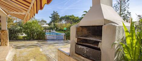 An outdoor patio with a stone floor, a barbecue grill, and a pool in the background.