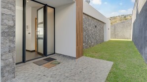 A modern house with a stone exterior, a glass door entrance, and a small grassy yard. - Casa Mozart II (Calheta)