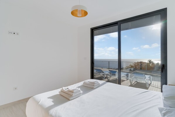 A modern hotel room with a large balcony, a bed with neatly folded towels, and a view of the sea and beach. - Casa Mozart II (Calheta)
