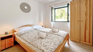 Un lit bien fait, recouvert d’une couvre-lit à motifs, une lampe de chevet et une fenêtre donnant sur un paysage verdoyant.