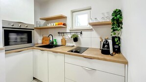 Une cuisine moderne avec des armoires blanches, un plan de travail noir, un four encastré, un évier et une fenêtre située au-dessus du plan de travail.