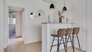 Eine moderne Küche mit weißem Holzvertäfelung, zwei Pendelleuchten, einer Bar mit Barhocker und Blick in den angrenzenden Essbereich.