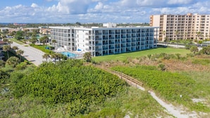 A modern hotel with multiple floors, a swimming pool, and a well-maintained lawn. - Direct Oceanfront Condo W/ Private Balcony, Heated Pool & Spa-like Hot Tub ☀️ (Cape Canaveral)