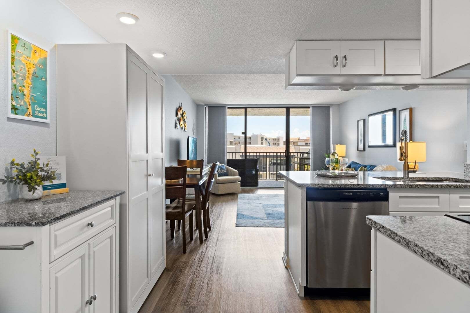 A modern kitchen with a central island, a dining area with a sofa, and a view of the cityscape through large windows.