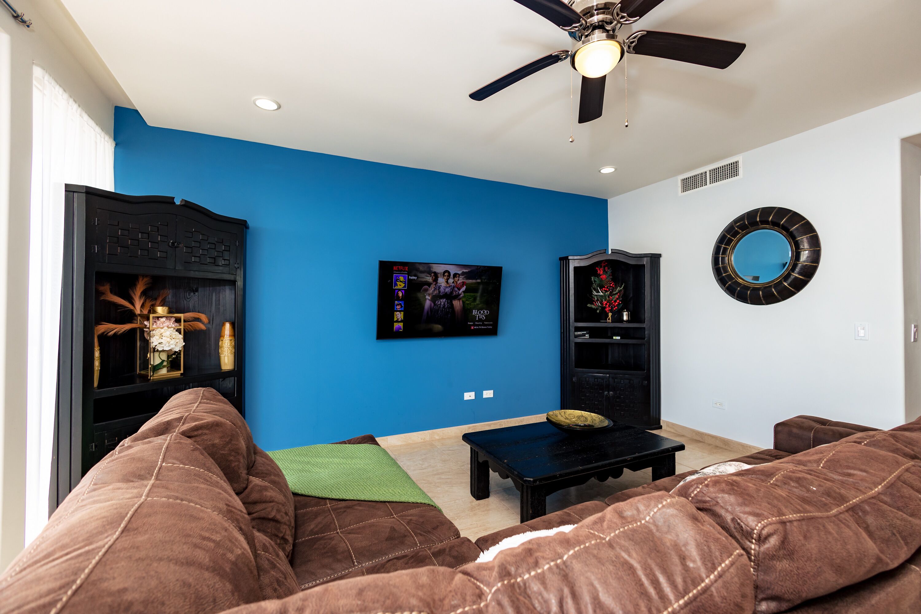Ein Wohnzimmer mit blauer Wand, Deckenventilator, Flachbildfernseher und Kamin.