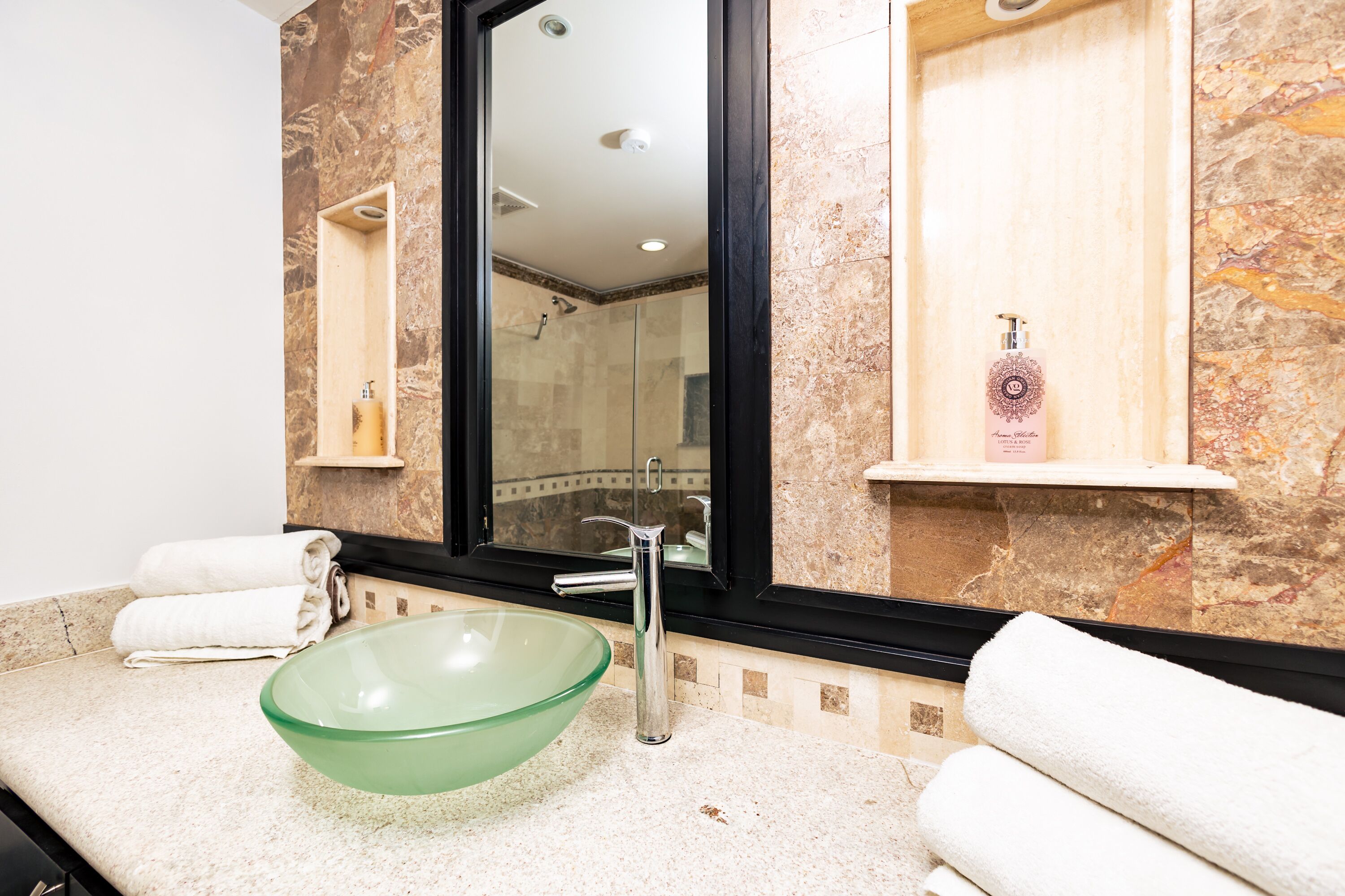 A bathroom with a glass bowl sink, a large mirror, and a shower area.
