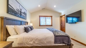 Een slaapkamer met een groot bed, een wandtelevisie, een raam met zonwering en een schilderij aan de muur.