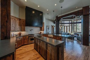 A spacious kitchen with wooden cabinets, a large island, and a dining area with a view. - Abode at Northside, ski-in/ski-out, hot tub, mountain views (Park City)