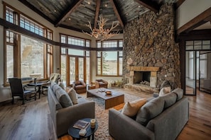 A spacious living area with a stone fireplace, large windows, and a high ceiling.