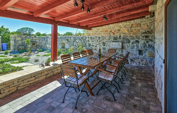 An outdoor patio with a stone wall, wooden table, and chairs.