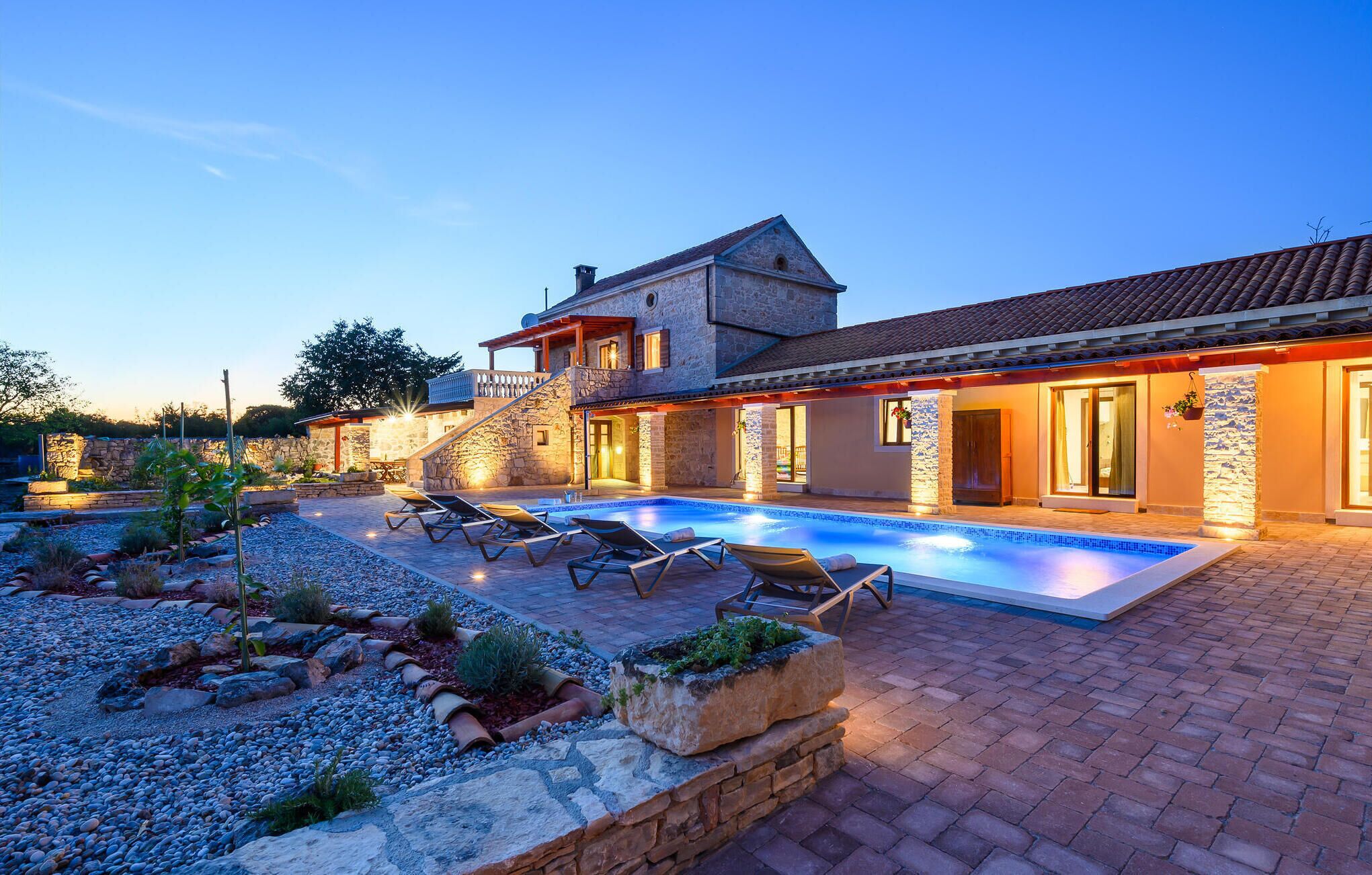 Una casa de piedra con piscina, sillones de descanso y un jardín cuidado.