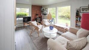 Ein gemütliches Wohnzimmer mit Fernseher, Korbmöbeln, Kamin und Blick ins Freie.