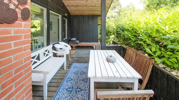 Eine Terrasse mit weißer Holzmöbelgruppe, darunter Bänke und ein Tisch, sowie einem blauen, gemusterten Teppich.