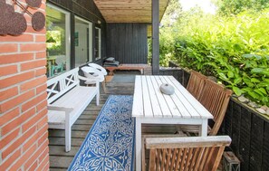 Une terrasse dotée de meubles en bois peints en blanc, notamment des bancs et une table, ainsi qu’un tapis bleu à motifs.