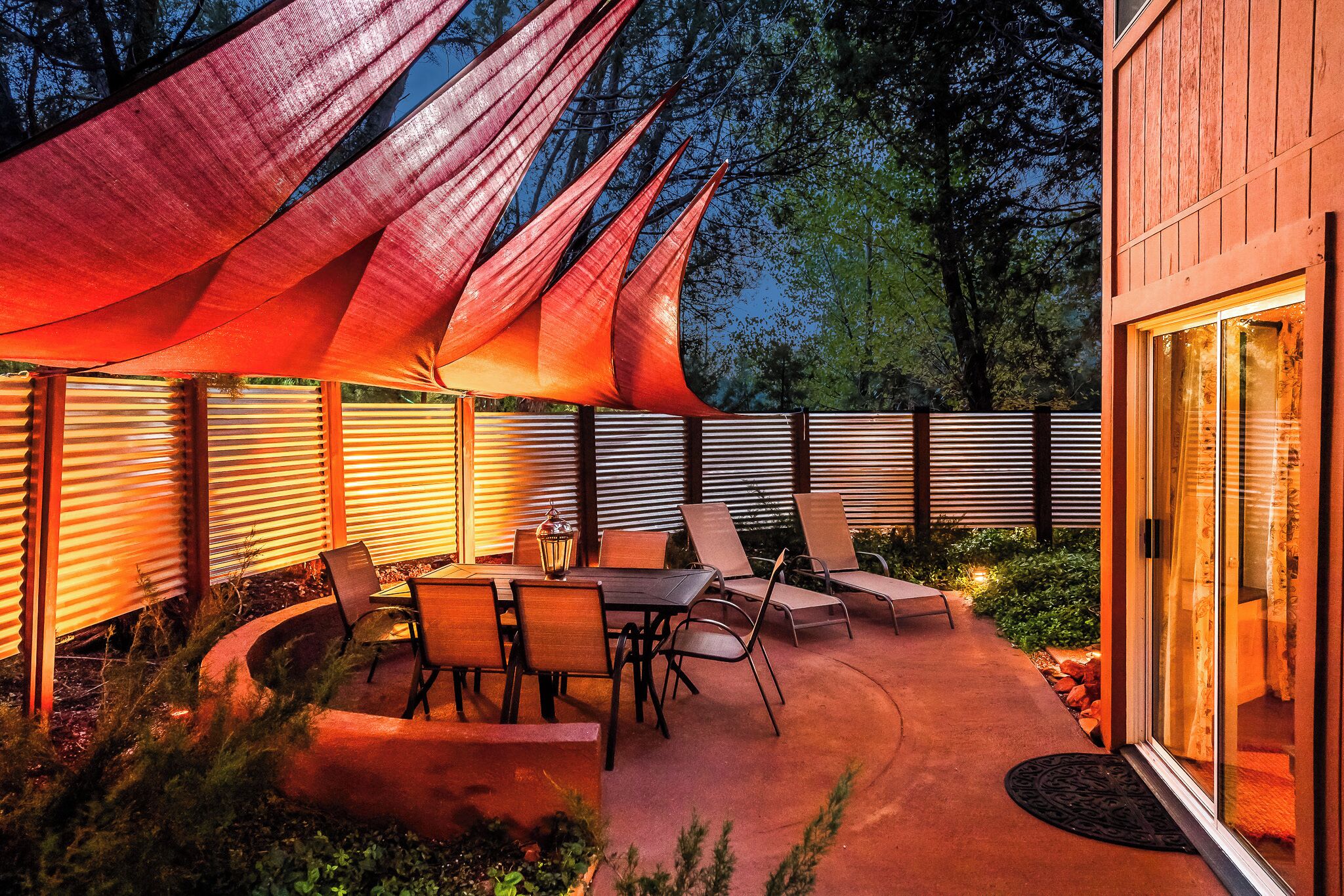 An outdoor patio with a table and chairs, surrounded by a wooden fence and a large red canopy.