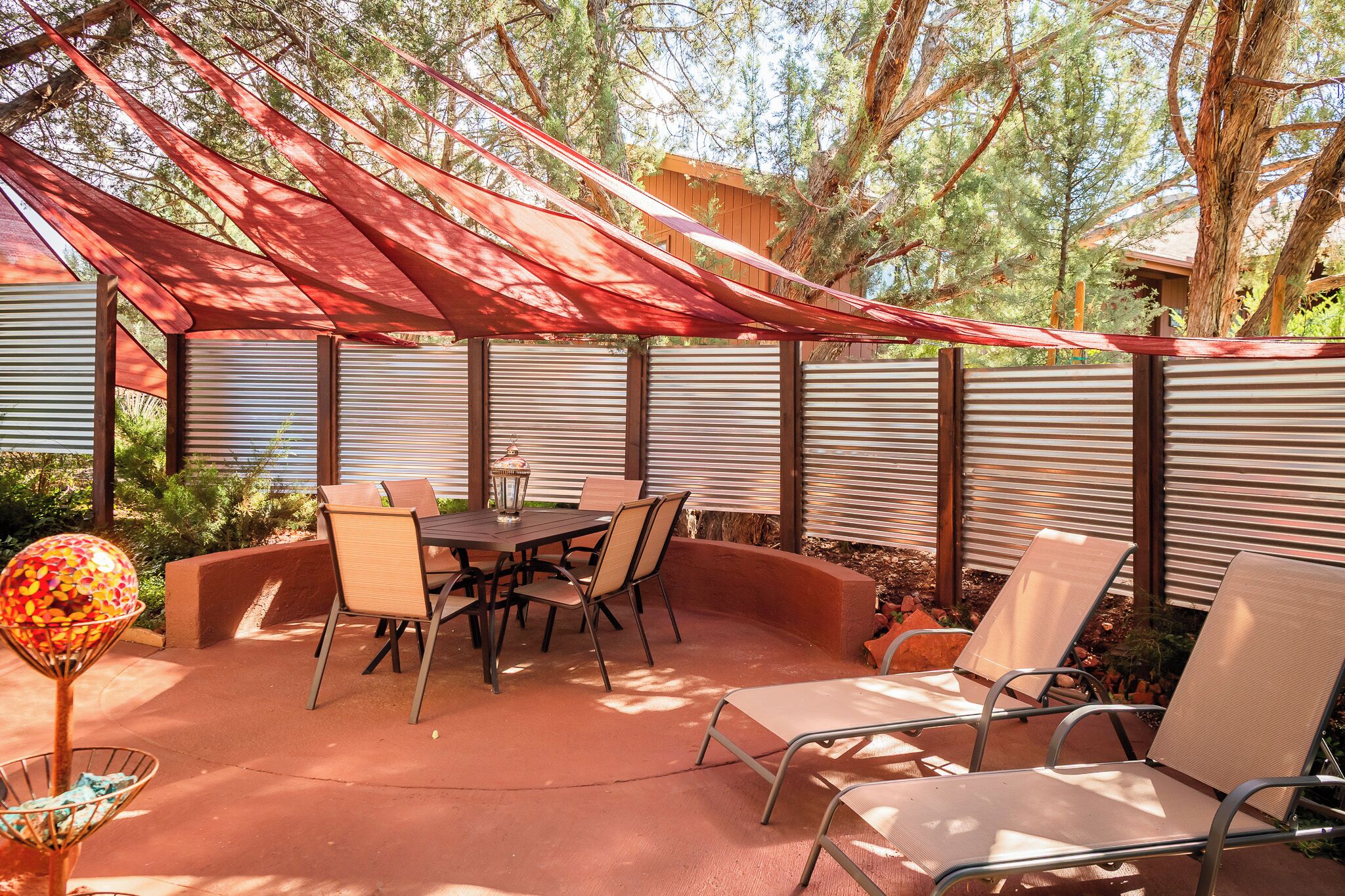 Eine Terrassenfläche im Freien mit Tisch und Stühlen, umgeben von einem roten Baldachin und Metallrollos.