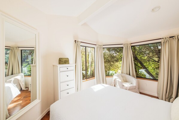 Un dormitorio con una cama grande, un aparador, una silla y un ventanal con cortinas.