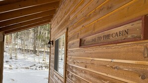 A wooden cabin with a 'WELCOME TO THE CABIN' sign, a wooden deck, and a snowy forest view. - Pool-Table Game Room, Darts & Starlink - Pet-Friendly, Mtn Views (Fairplay)