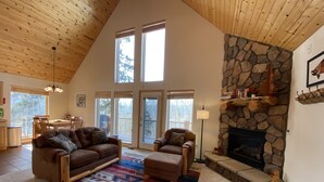 A spacious living room with a high ceiling, a stone fireplace, and a large window overlooking a deck. - Pool-Table Game Room, Darts & Starlink - Pet-Friendly, Mtn Views (Fairplay)