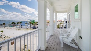 Un balcon donnant sur la plage, avec des balustrades blanches, une terrasse en bois et trois fauteuils Adirondack.