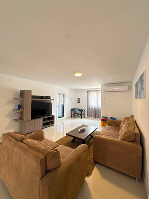 A living room with two sofas, a coffee table, a TV, and a pool table.