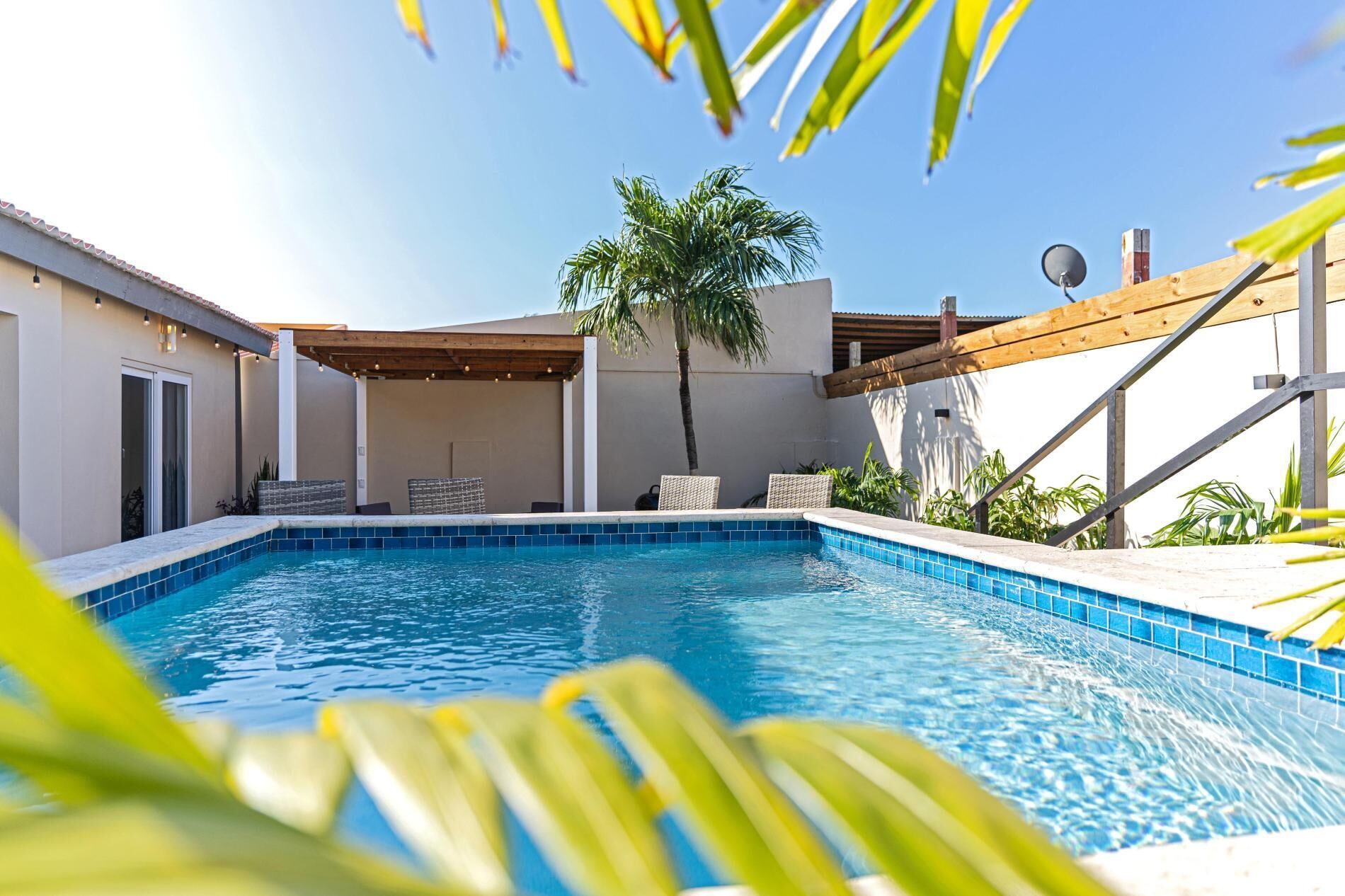 Une piscine dont le bord est revêtu de carreaux, entourée d’un patio abrité avec des sièges.