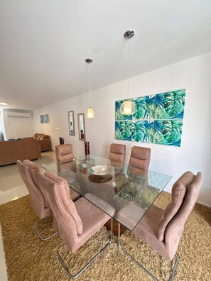 A modern dining area with a glass table, cushioned chairs, and a tropical-themed wall art.