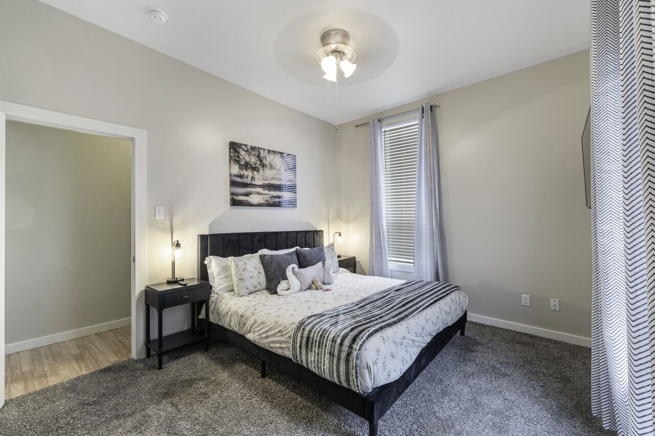 A bedroom with a bed, bedside tables, a ceiling light, a window with blinds, and a wall-mounted artwork.
