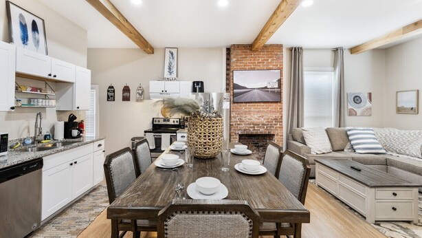 Una cocina moderna con gabinetes blancos, una mesa de comedor para cuatro personas y una chimenea de ladrillo.