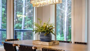 Een eetgedeelte met een houten tafel, zwarte geweven stoelen, een potplant en een hanglamp.