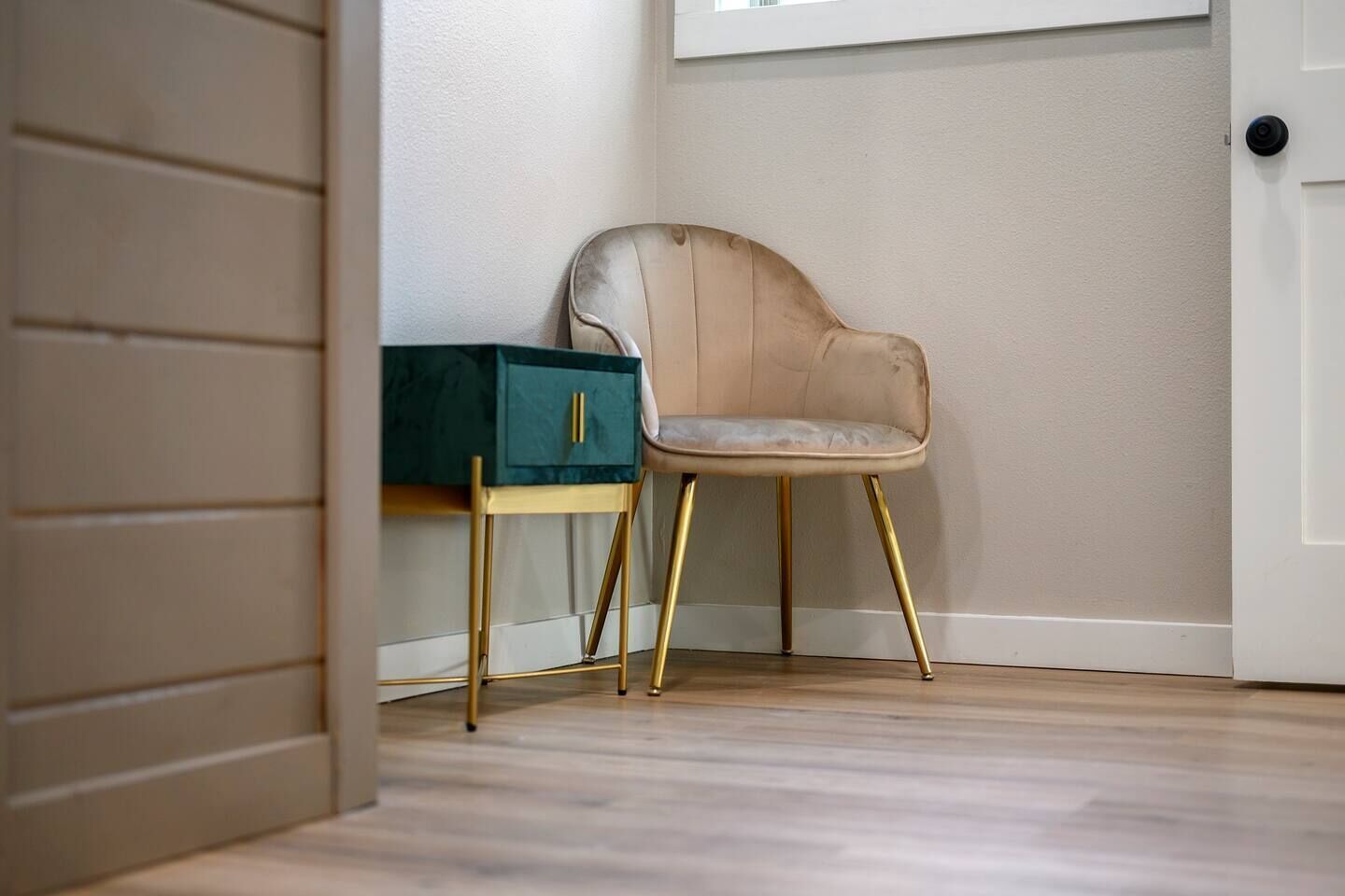 Una silla con asiento y respaldo acolchados, una mesita con un cajón verde y una puerta blanca con pomo negro.