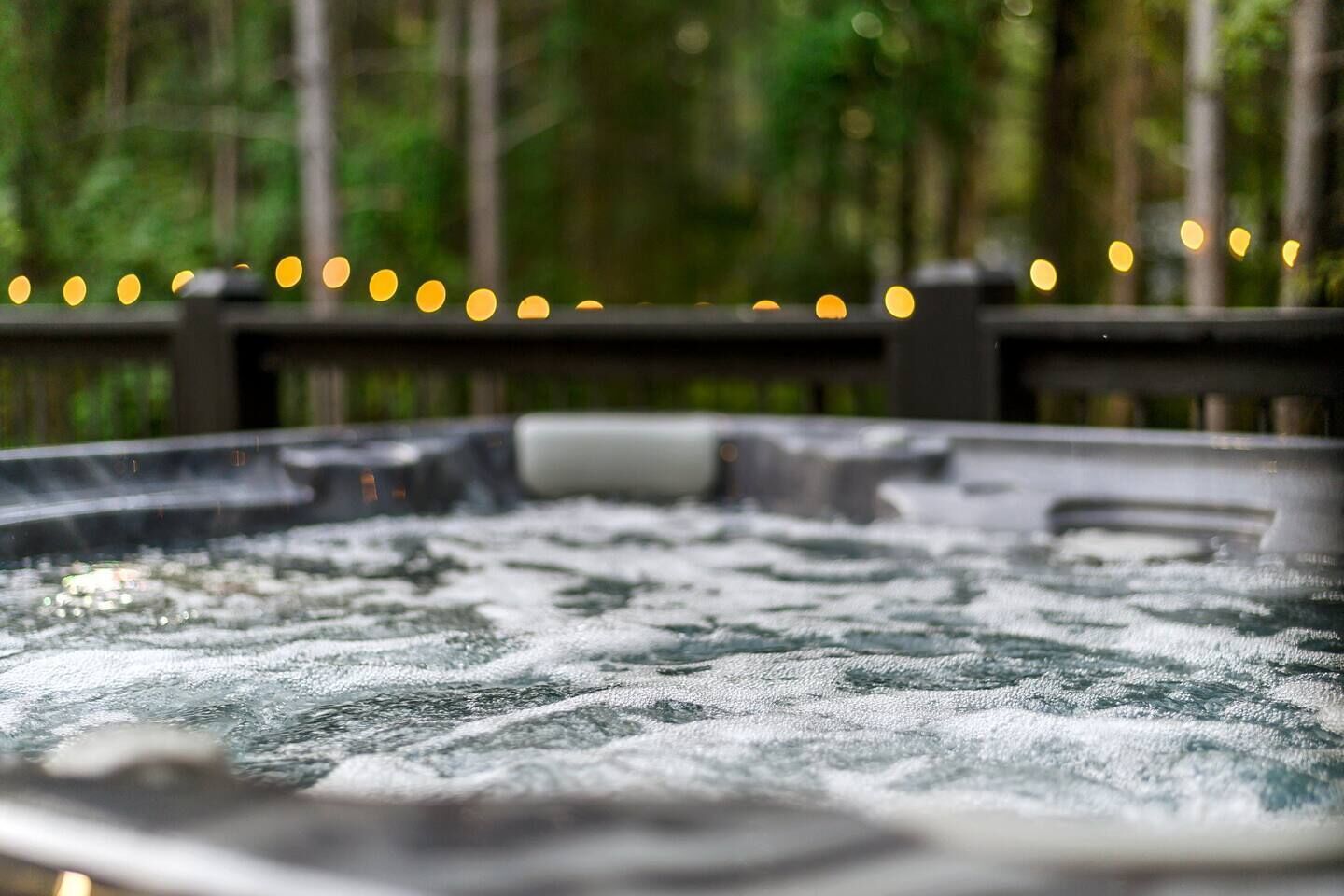 Un jacuzzi con cubierta de madera y luces colgantes al fondo.