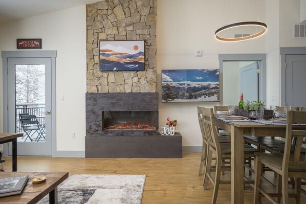 Una sala de estar con chimenea de piedra, un comedor con mobiliario de madera y un cuadro grande sobre la chimenea.