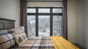 A bedroom with a bed, a window with curtains, and a view of a snowy landscape.