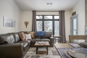 Uma sala de estar com sofá de couro, uma mesa de centro, uma mesinha lateral e um espaço de jantar com mesa e cadeiras.