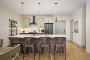 Uma cozinha moderna com ilha central, banquetas e iluminação pendente.