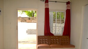 Una habitación con un sofá de cuero marrón, una ventana con cortinas rojas y una puerta que da al exterior.