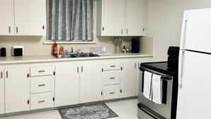 Una cucina con pensili bianchi, una finestra con tende, un forno in acciaio inossidabile e un frigorifero.
