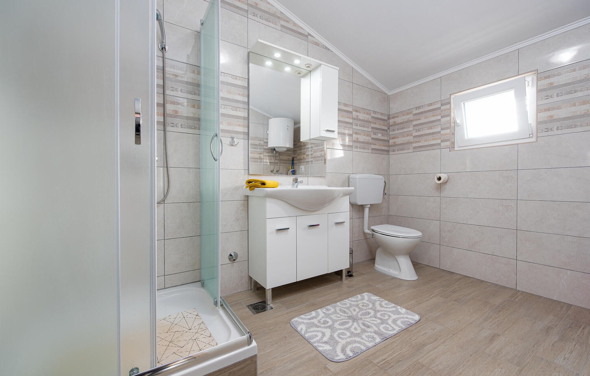 Ein modernes Badezimmer mit einer Duschkabine aus Glas, einem weißen Waschbecken, einer Toilette und einem gemusterten Teppichboden.